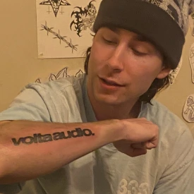 Oscar Harold showing a voltaaudio. tattoo on his forearm