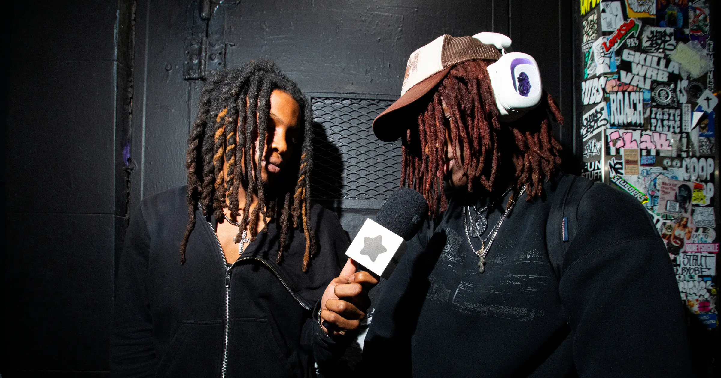 Two people backstage, one wearing white Volta Audio headphones, being interviewed