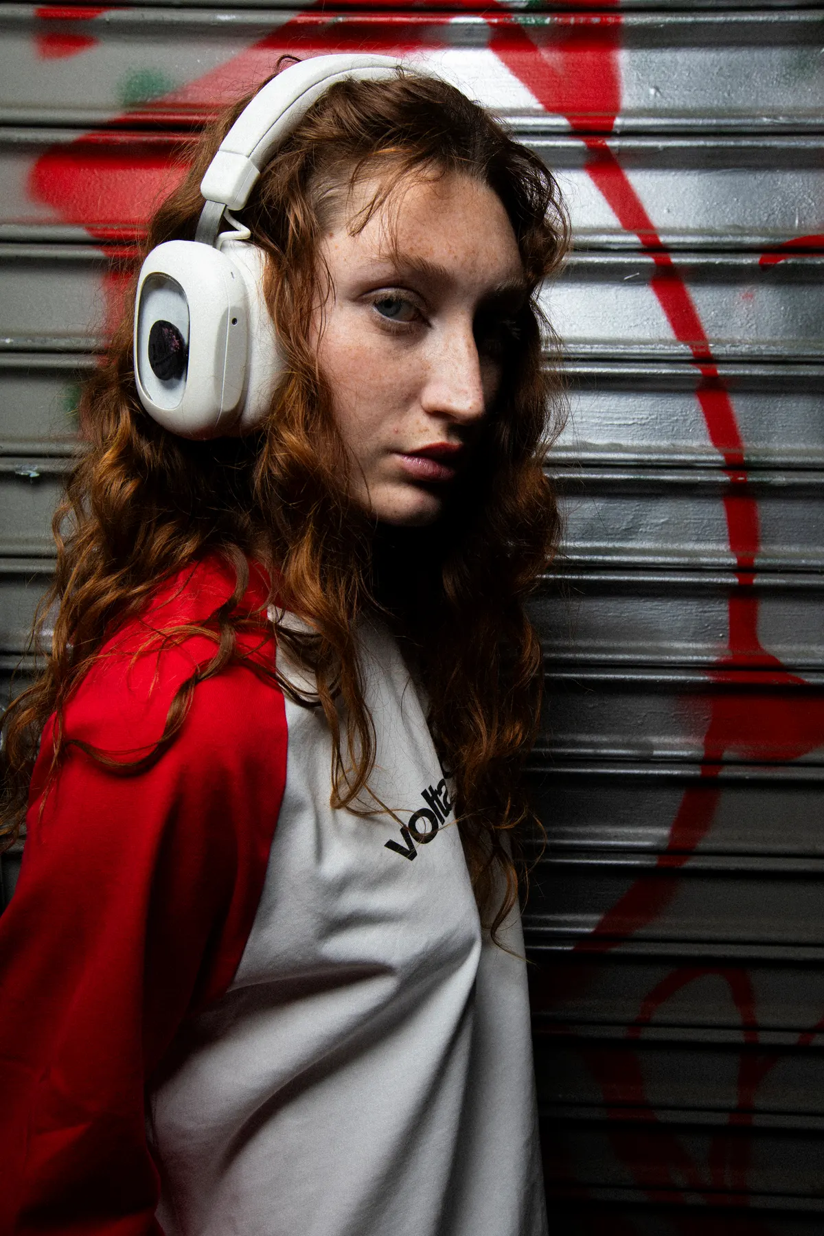 Person wearing white Volta Audio headphones against a graffitied shutter