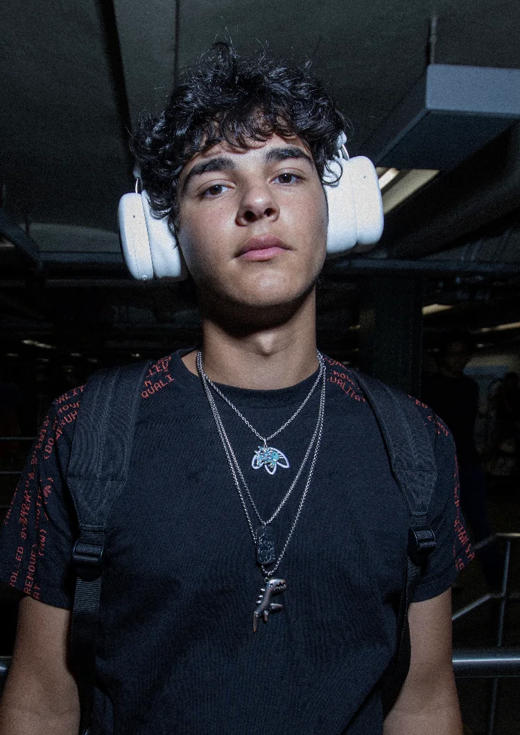 Person in a black tee and silver chains wearing white Volta Audio headphones in a subway station